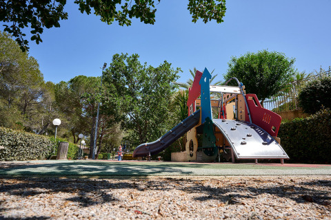 Playground with slide and climbing structure among trees at Camping Leï Suves, Provence-Alpes-Côte d’Azur, France.