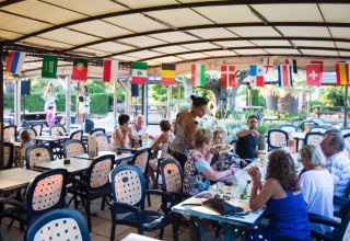 Buitenrestaurant op Camping Leï Suves in Frankrijk, met etende gasten en vlaggen van verschillende landen.