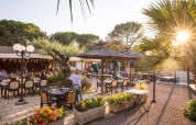 Zona de comedor al aire libre en Camping Leï Suves, Provenza, con palmeras, flores y comensales felices.