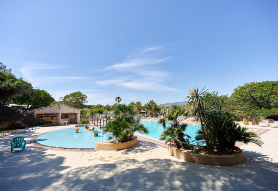 Buitenzwembad met palm- bomen en ligstoelen bij Camping Leï Suves in Provence-Alpes-Côte d’Azur, Frankrijk.