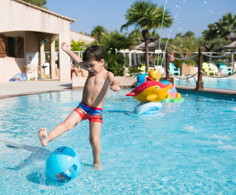 Bambino calcia una palla in piscina presso Camping Leï Suves, Provenza-Alpi-Costa Azzurra, Francia.