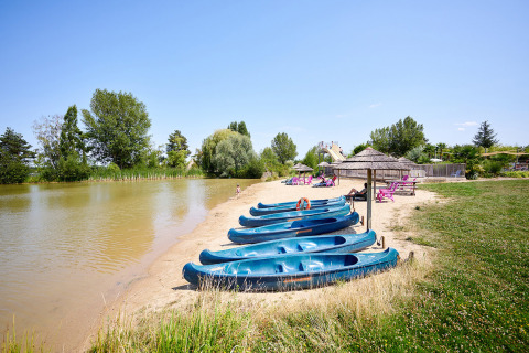 Sandy lakeside beach at Camping Les Bois du Bardelet in France, with blue canoes and relaxing visitors.