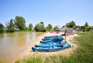 Sandy lakeside beach at Camping Les Bois du Bardelet in France, with blue canoes and relaxing visitors.