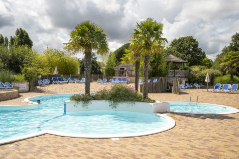 Piscina con palmeras y tumbonas en Camping Les Bois du Bardelet, Centre-Val de Loire, Francia, bajo un cielo nublado.