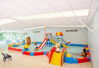 Overdekt kinderbad met kleurrijke glijbanen en speeltoestellen op Camping Les Bois du Bardelet in Frankrijk.