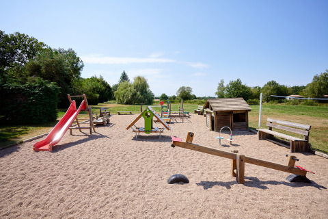 Parque infantil con tobogán rojo, columpios y casita de madera en Camping Les Bois du Bardelet, Centro-Val de Loire, Francia.