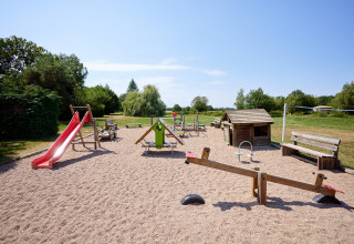 Playground with red slide, swings and wooden playhouse at Camping Les Bois du Bardelet in Centre-Val de Loire, France.