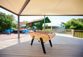 Outdoor foosball table under canopy at Camping Les Bois du Bardelet, surrounded by greenery and seating.