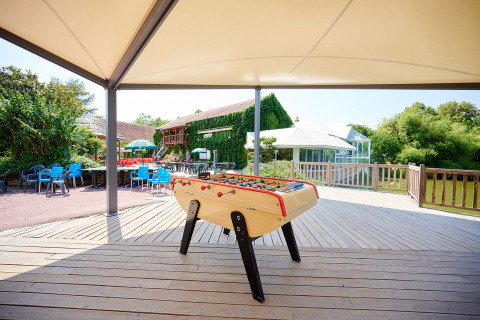Table de baby-foot en plein air sous abri au Camping Les Bois du Bardelet, entourée de verdure et de sièges.