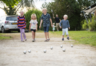Fire børn leger petanque på en grusvej på Camping Les Bois du Bardelet i Centre-Val de Loire, Frankrig.