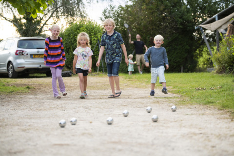 Fire børn leger petanque på en grusvej på Camping Les Bois du Bardelet i Centre-Val de Loire, Frankrig.