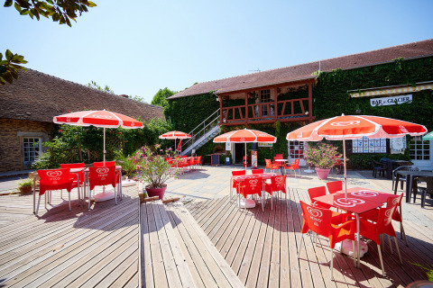 Terraza al aire libre con sombrillas rojas en Camping Les Bois du Bardelet, Centre-Val de Loire, Francia.