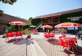 Udendørs terrasse med røde parasoller og borde på Camping Les Bois du Bardelet i Centre-Val de Loire, Frankrig.