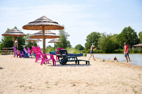 Strandszene im Camping Les Bois du Bardelet, Frankreich, mit bunten Stühlen, Sonnenschirmen und spielenden Leuten.