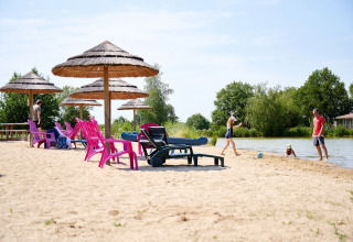Strandscène bij Camping Les Bois du Bardelet, Frankrijk, met kleurrijke stoelen, parasols en spelende mensen.