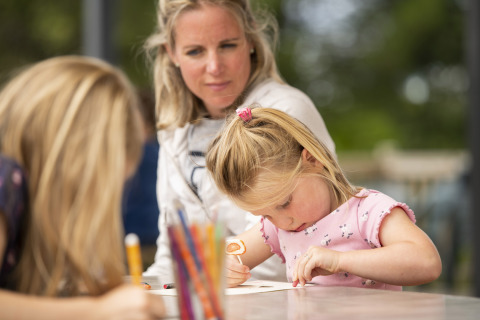 Una niña dibuja en una mesa bajo la mirada de una mujer en Camping Les Bois du Bardelet, Francia.