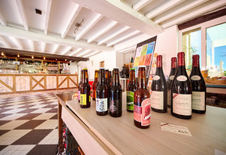Selectie wijn- en bierflessen uitgestald op een tafel in een moderne bar bij Camping Les Bois du Bardelet, Frankrijk.