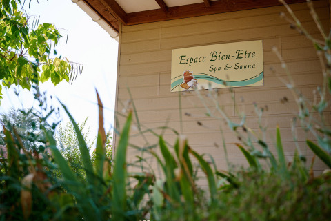 Cartel de 'Espace Bien-Etre Spa & Sauna' en Camping Les Bois du Bardelet, rodeado de vegetación.