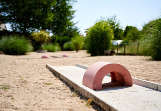 Minigolfbane med buet forhindring, omgivet af sand og grønne planter hos Camping Les Bois du Bardelet, Frankrig.