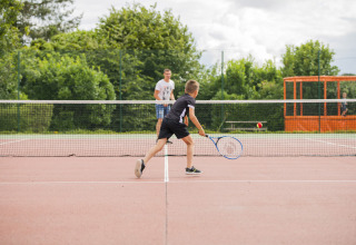 Niño jugando al tenis en cancha exterior en Camping Les Bois du Bardelet, Centre-Val de Loire, Francia.