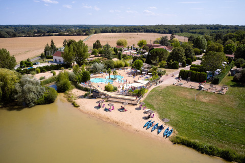 Aerial view of Camping Les Bois du Bardelet shows a pool, sandy beach, kayaks, and green landscape in France.