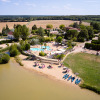 Aerial view of Camping Les Bois du Bardelet shows a pool, sandy beach, kayaks, and green landscape in France.