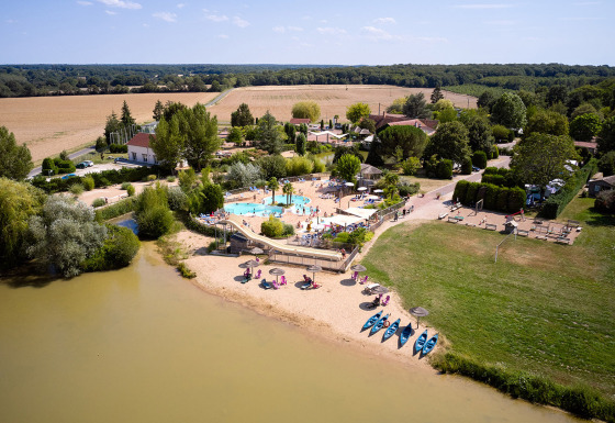 Aerial view of Camping Les Bois du Bardelet shows a pool, sandy beach, kayaks, and green landscape in France.