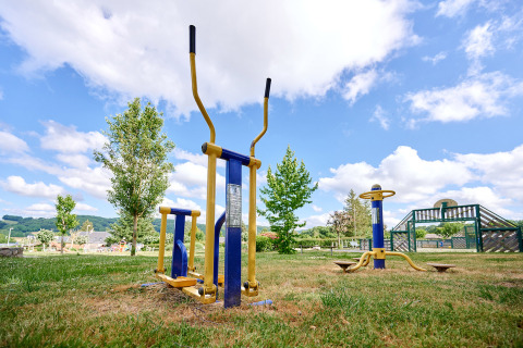 Outdoor gym equipment set up on grass at Camping Les Genêts holiday park in Occitanie, France, under blue skies.