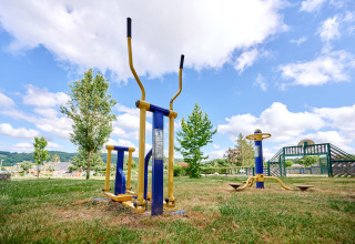 Buitensporttoestellen op het gras bij Camping Les Genêts, een vakantiepark in Occitanie, Frankrijk, onder blauwe luchten.
