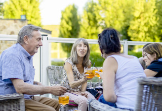 Fire voksne nyder drinks og samtale udendørs ved Camping Les Genêts feriepark i Occitanie, Frankrig.