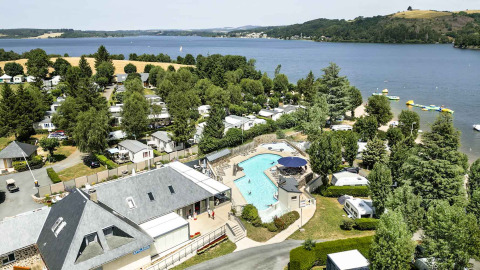Holiday photo at Camping Les Genêts in Occitanie, France, showing a pool, lake, and mobile homes.