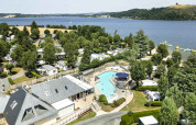 Photo de vacances au Camping Les Genêts en Occitanie, France, montrant une piscine, un lac et des mobil-homes.