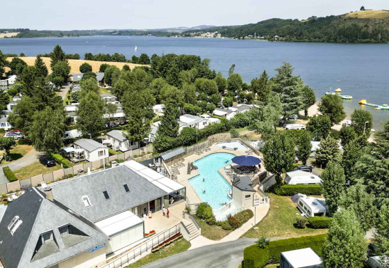 Urlaubsbild vom Camping Les Genêts in Occitanie, Frankreich, mit Pool, See und zahlreichen Mobilheimen.