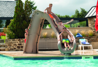 Children playing on a waterslide by the pool at Camping Les Genêts holiday park in Occitanie, France.