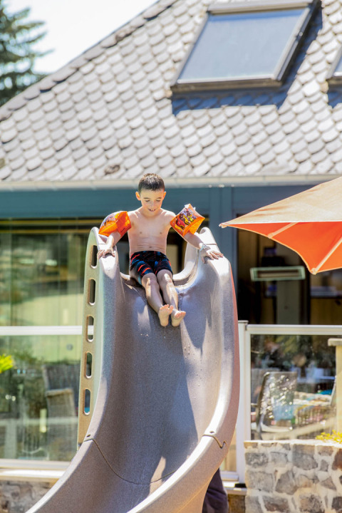 Bambino con braccioli scivola su uno scivolo al Camping Les Genêts, parco vacanze in Occitanie, Francia.