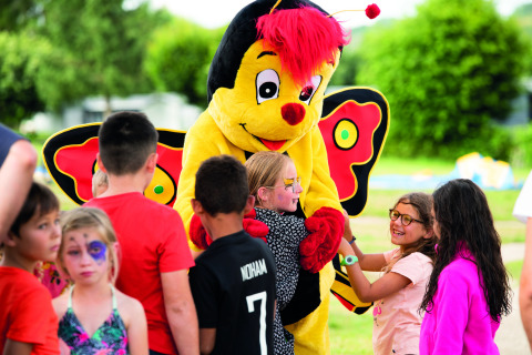 Bambini giocano e abbracciano una mascotte farfalla al Camping Les Genêts in Occitania, Francia.