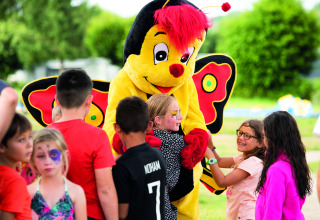 Bambini giocano e abbracciano una mascotte farfalla al Camping Les Genêts in Occitania, Francia.