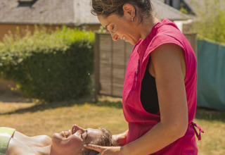 Kvinde får afslappende hovedmassage af terapeut udendørs på Camping Les Genêts i Occitanie, Frankrig.