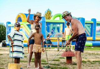 Familie, der spiller minigolf på Camping Les Genêts i Occitanie, Frankrig, med farverigt oppusteligt legeområde.