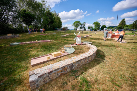 Personas jugando mini golf en Camping Les Genêts, un parque vacacional en Occitanie, Francia, en un día soleado.