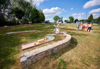Folk spiller minigolf på Camping Les Genêts i Occitanie, Frankrig under blå himmel og grønne træer.