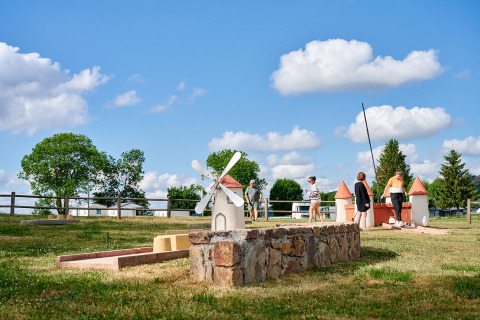 Camping Les Genêts en Occitania, Francia, con personas jugando minigolf en un campo verde bajo cielo azul.