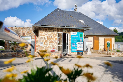 Recepción del Camping Les Genêts en Occitania, Francia, edificio de piedra con flores en primer plano.