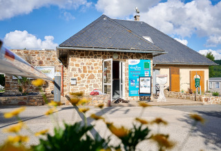 Rezeption des Campingplatzes Les Genêts in Occitanie, Frankreich, mit Steinwänden und Blumenvordergrund.