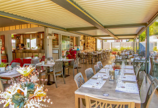 Lyst og moderne restaurantområde med dagslys, dækket borde og udsigt over terrassen på Camping Les Genêts.
