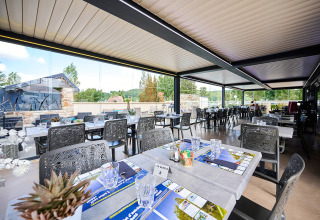 Covered outdoor dining area at Camping Les Genêts in Occitanie, France, with modern tables and chairs.
