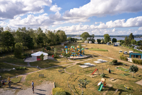 Aerial view of Camping Les Genêts holiday park in Occitanie, France, with playground, green spaces and lake view.