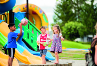 Kinder spielen auf einem farbenfrohen Spielplatz im Ferienpark Camping Les Genêts in Occitanie, Frankreich.