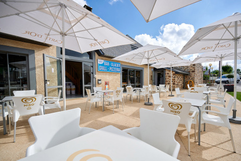 Terrasse extérieure avec chaises et parasols blancs au Camping Les Genêts en Occitanie, France, ciel bleu.