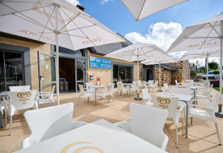 Terrasse extérieure avec chaises et parasols blancs au Camping Les Genêts en Occitanie, France, ciel bleu.